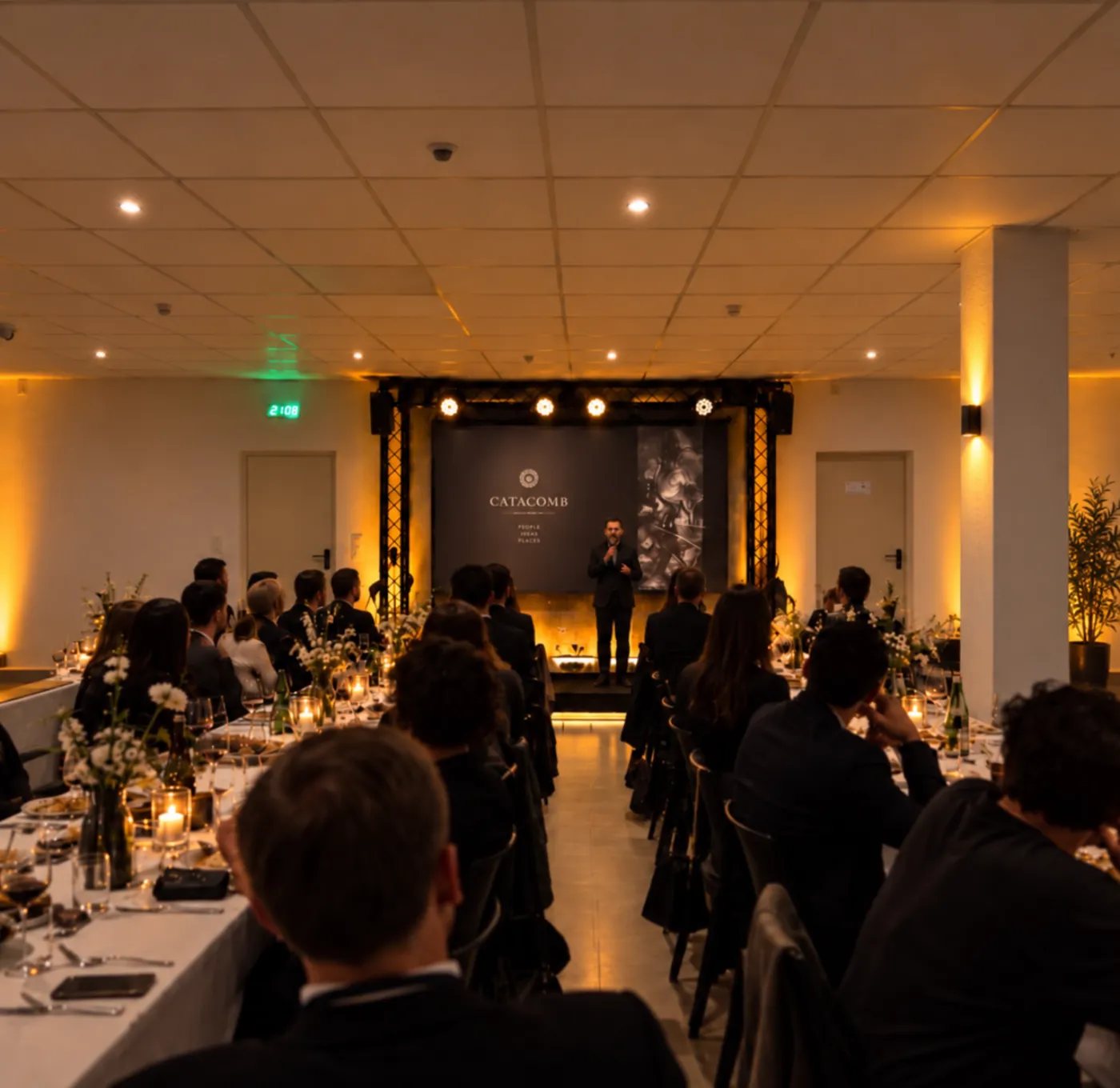 Gala-Dinner in der Halle mit langen, kerzenbeleuchteten Tafeln vor der Bühne mit Redner
