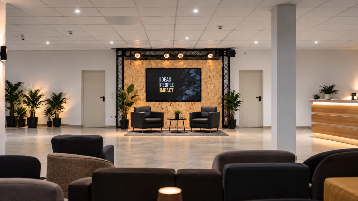 Bühne mit zwei Sesseln vor Holzwand und Bildschirm, davor Lounge-Sofas und Bar